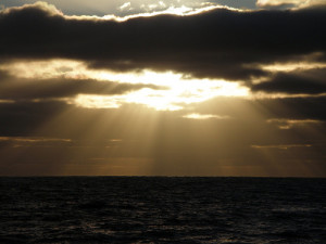 Sun breaking through clouds over sea